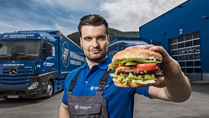 Ein Mann hält einen Burger vor einem Lastwagen.